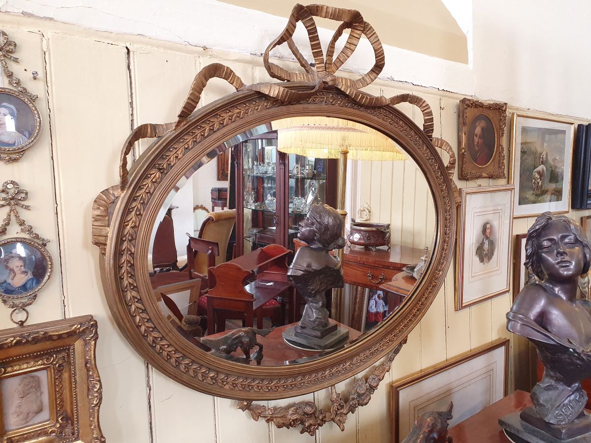 An antique Oval Gilt Gesso Framed Wall Mirror With Ribbon Pediment